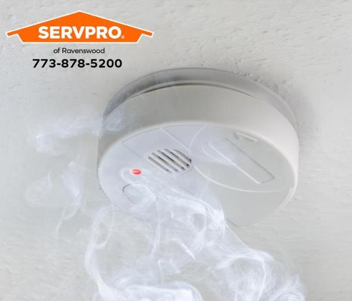 White smoke alarm with smoke on a white ceiling.