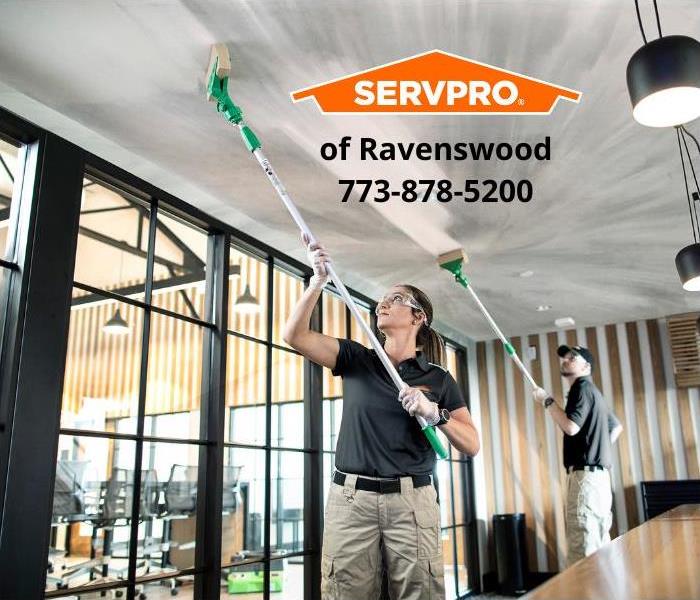Two SERVPRO employees wiping soot off of a ceiling in an office.